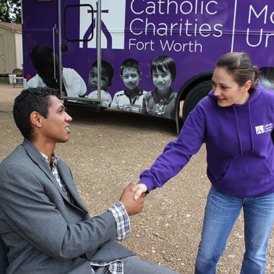 A Catholic Charities representative shakes the hand of a young man.