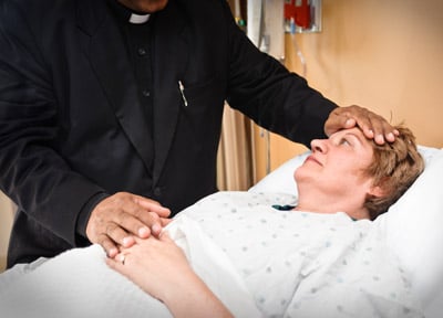 A priest visits and prays with a sick woman in the hospital.