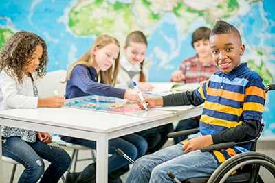 A young person in a wheelchair works on a school project with other students.