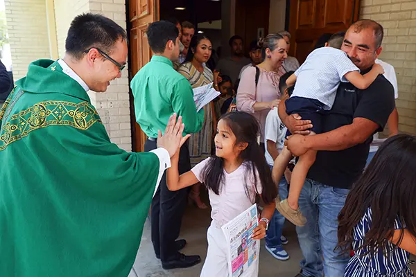 A priest gives a young girl a high five after Mass.