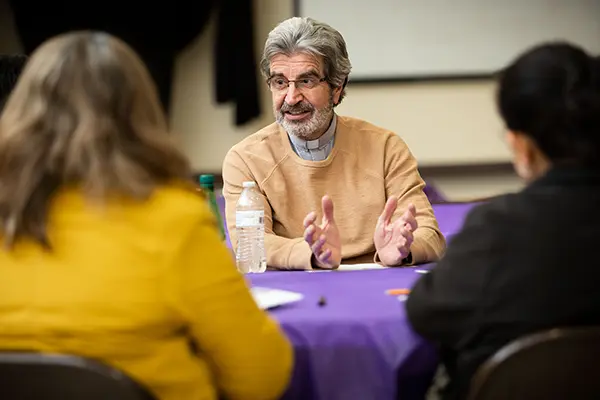 A priest talks to parishioners at a table.